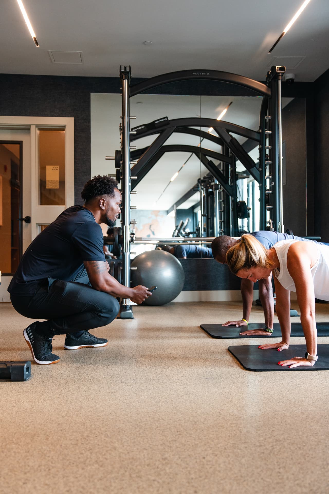 A trainer coaching two clients through a plank in a gym