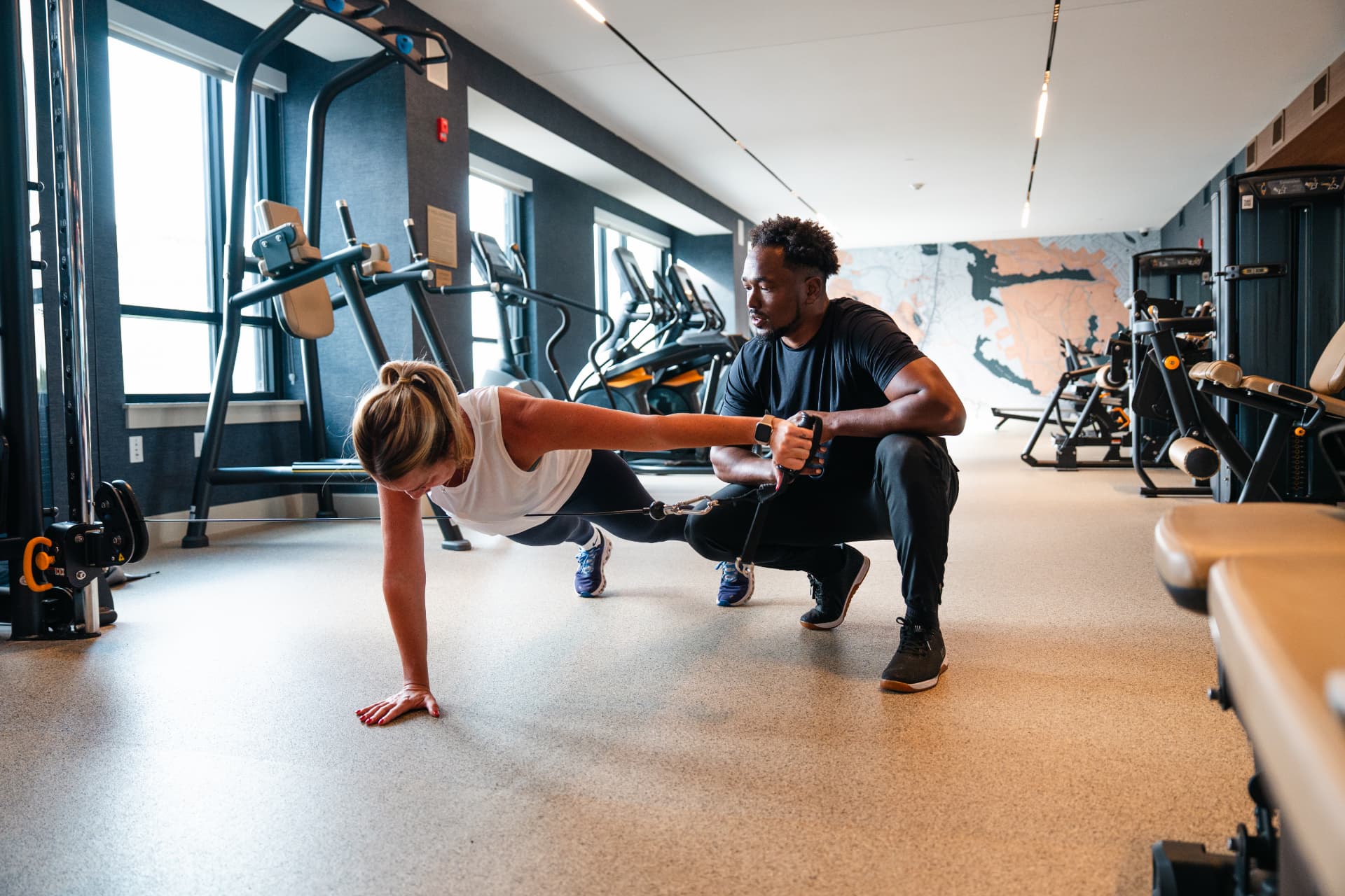 A trainer coaching a client through a cable exercise in a bright gym
